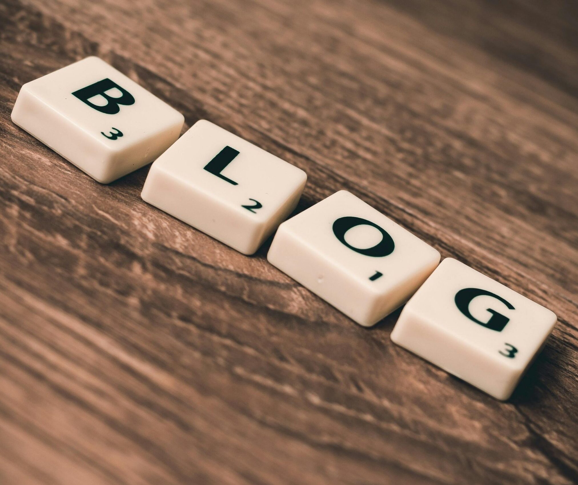Scrabble tiles spelling 'BLOG' on a wooden background, symbolizing creativity and writing.